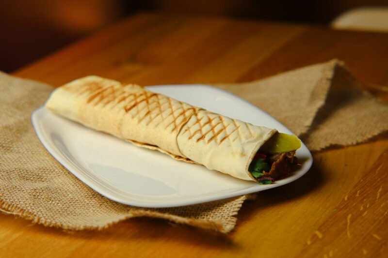 beef shoarma sandwich image Saj bread with chicken shawarma, pickle, garlic sauce, pomegranate sauce.